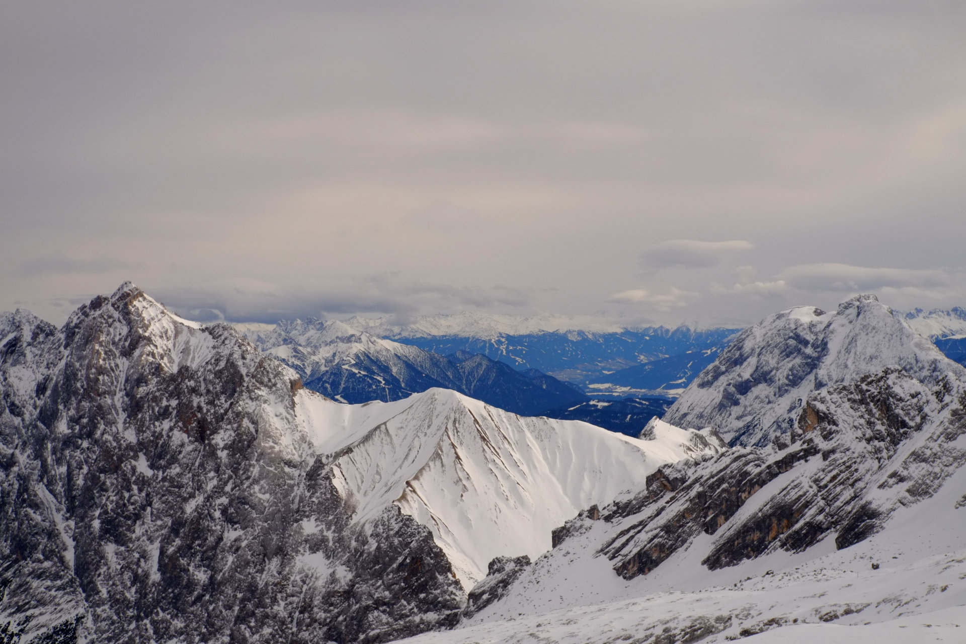 A photo of snowy rocky mountain peaks in the distance going continuing far away into the distance into the blue haze.