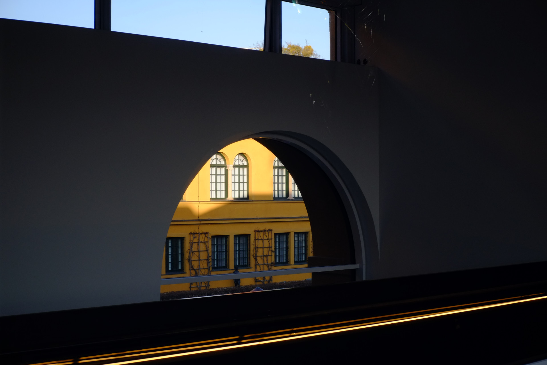 A photo of a hallway with an arch and a sunlit yellow building visible through the arch.