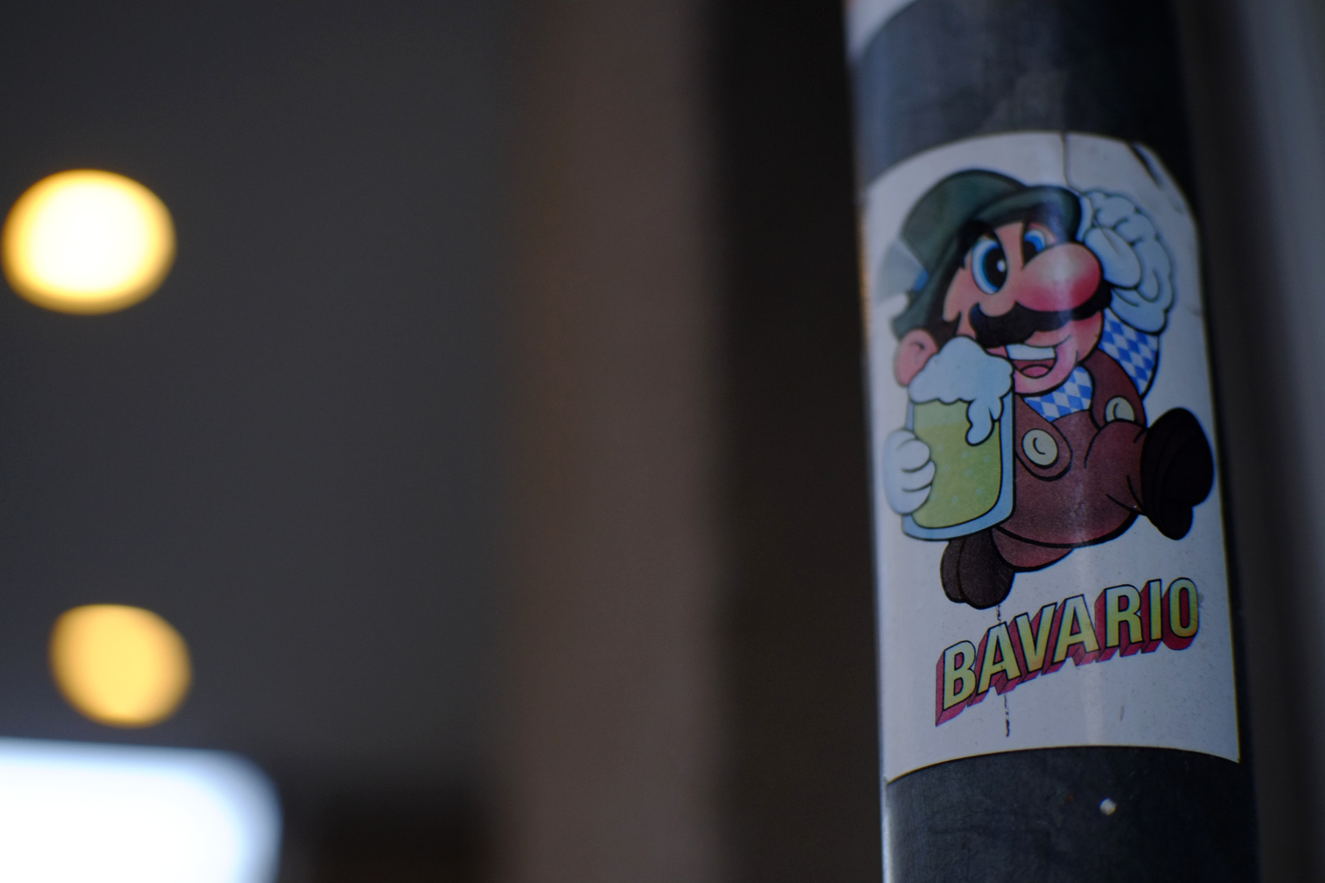 A photo of a sticker on a metal pole featuring Super Mario dressed in a traditional Bavarian costume with a glass of beer in his hand and with words BAVARIO under him.