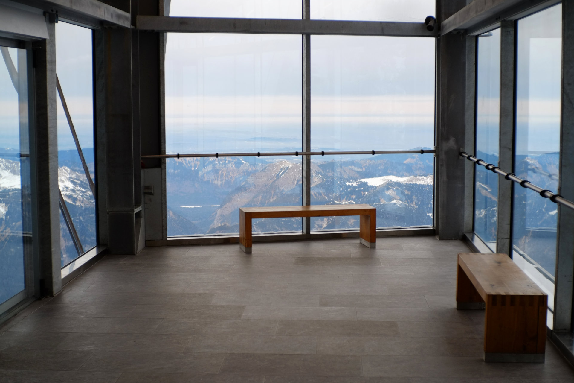 A photo of the end of a hallway with big windows instead of walls and two empty wooden benches.