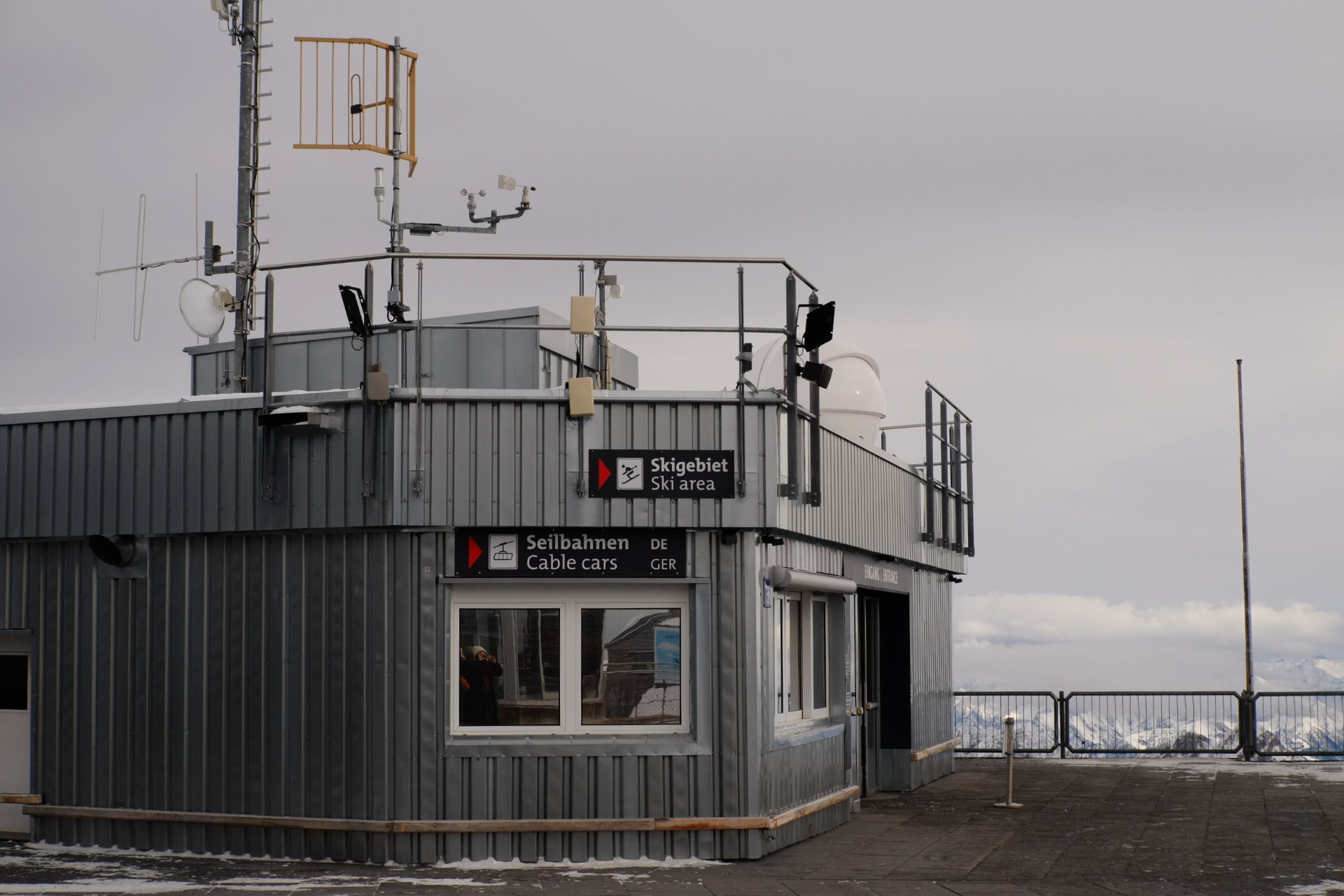 A photo of a grey metal booth on the observation deck with direction signs to the ski area and cable cars on one of its walls.