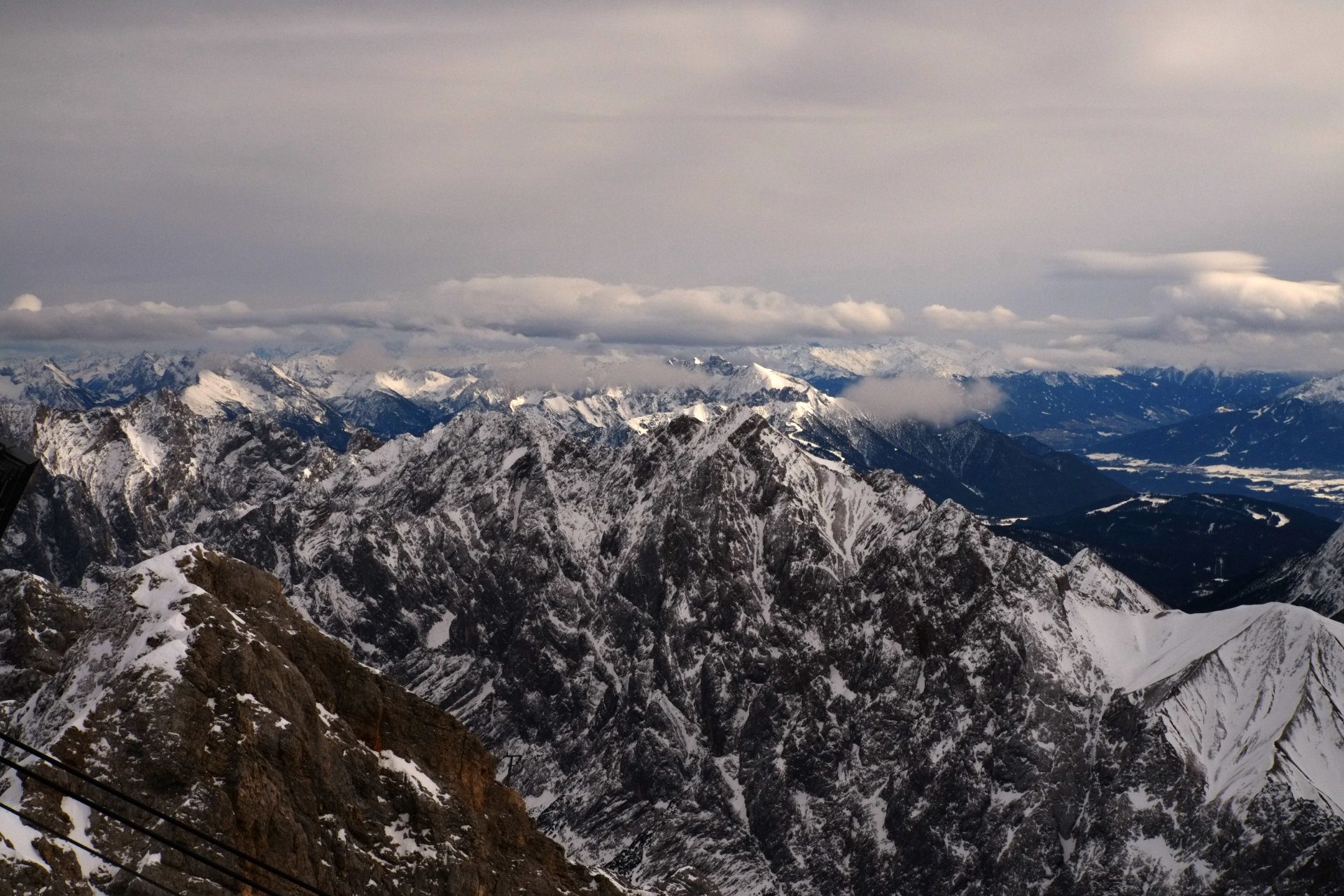 A photo of dark mountain peaks covered with snow and a layer of clouds above them, photo made from above