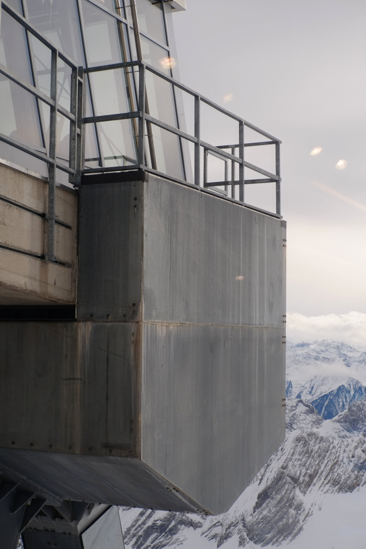 A photo of a metal platform foundation that hangs above white snowy mountains.