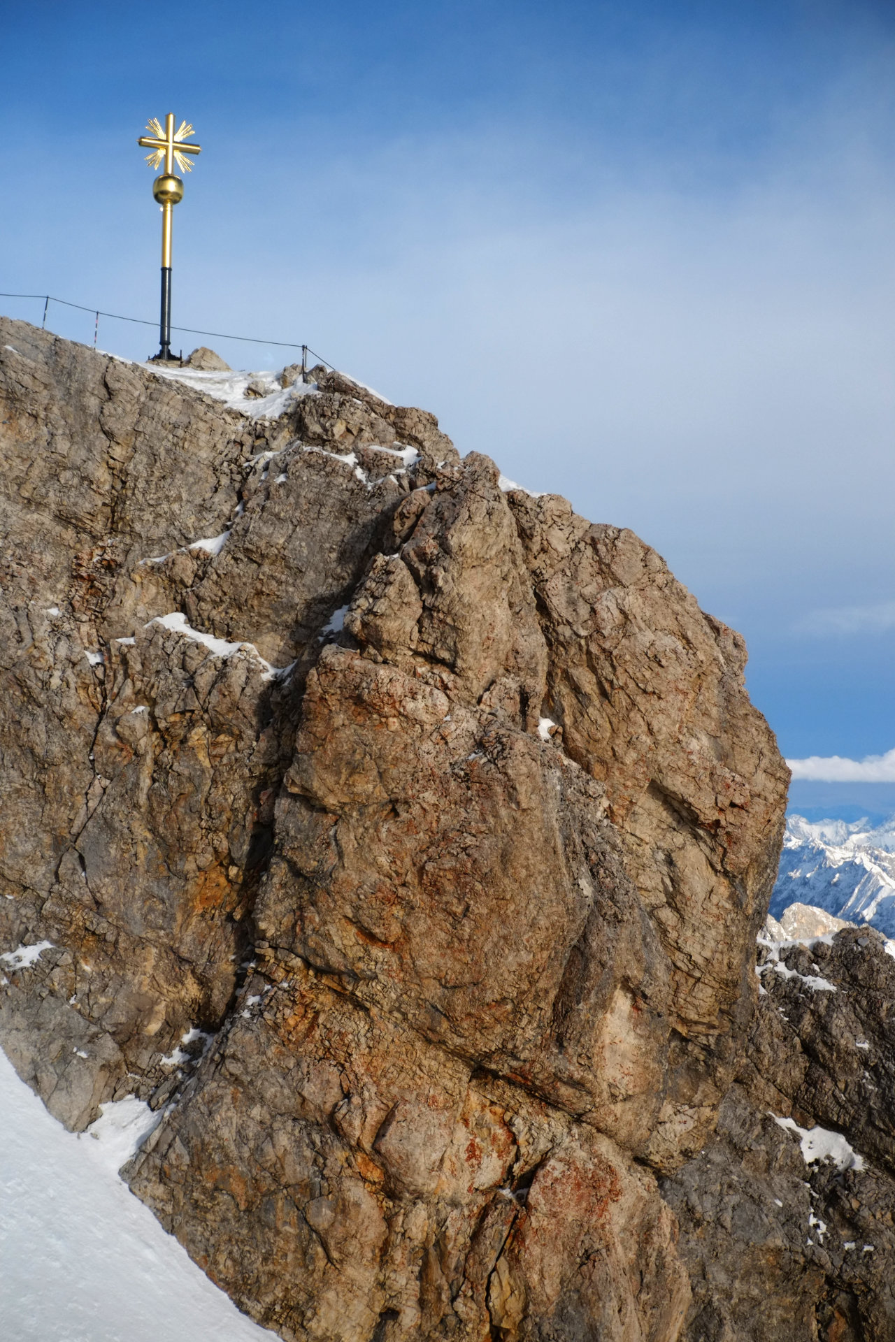 A photo of a brown rocky cliff illuminated by the evening sun with a golden cross on top of it.