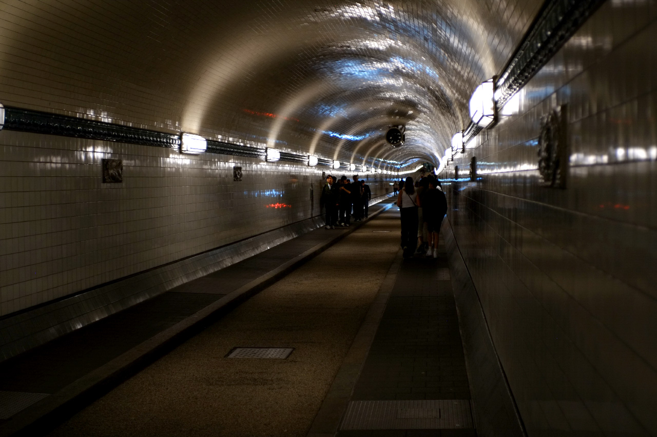 A photo inside Alter Elbtunnel. People are moving by the left and right sides of the tunnel, while the wider central road is used by cyclists.