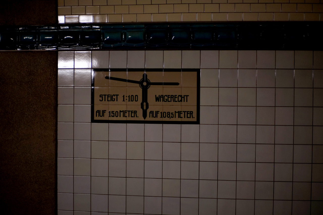 A photo of a yellow and black technical sign in the German language on one of the side of the tunnel. It says: STEIGT 1:100 WAGERECHT AUF 150 METER AUF 108.5 METER