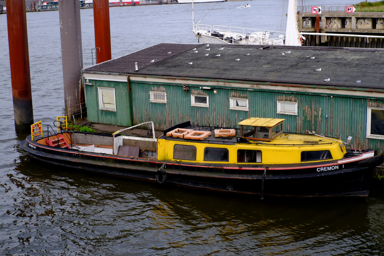 A photo of a yellow and black boat docked to a long green wooden building on water.