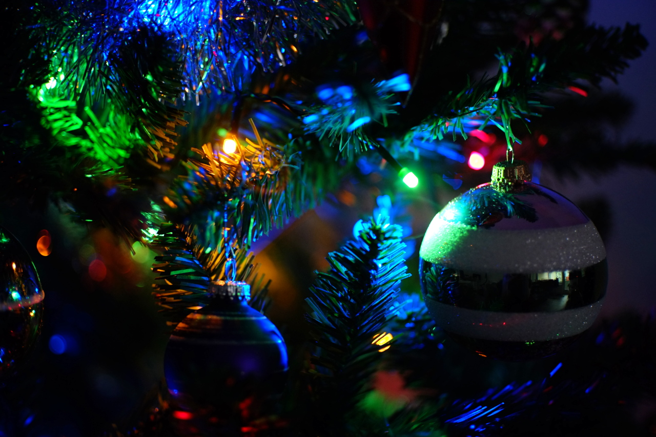 A close-up photo of plastic spruce  branches decorated with glass and plastic ornaments and electric garland lights shining through the branches.