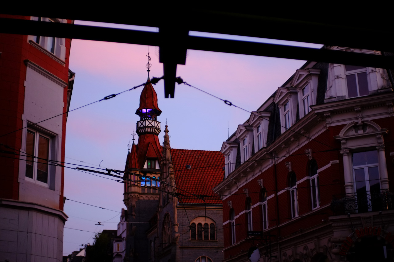 A photo of an old building with a pointed roof and a small tower with changing RGB lights shining from its windows.
