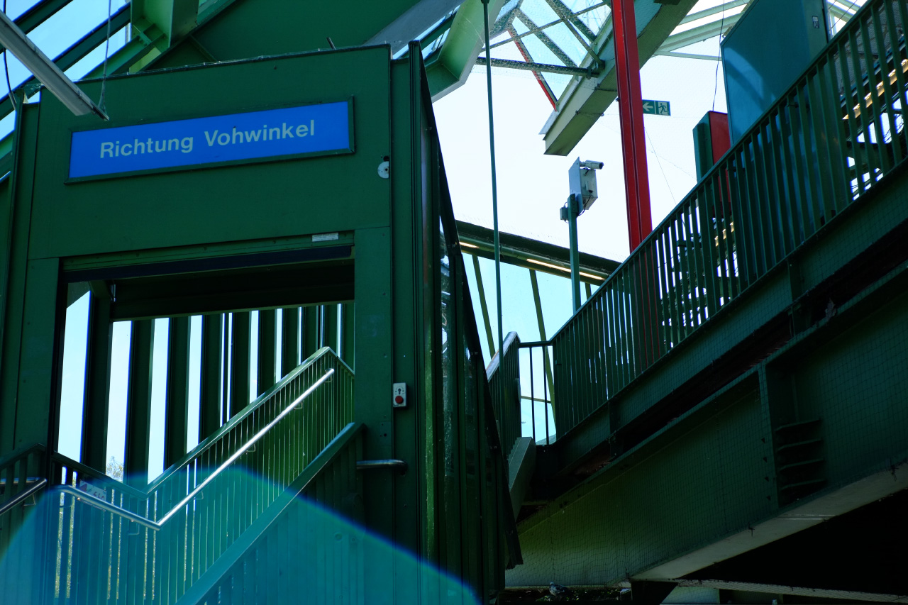 A photo of green metal stairs leading to a suspension railway station. The sign to the left says: Rightung Vohwinkel (Direction Vohwinkel)