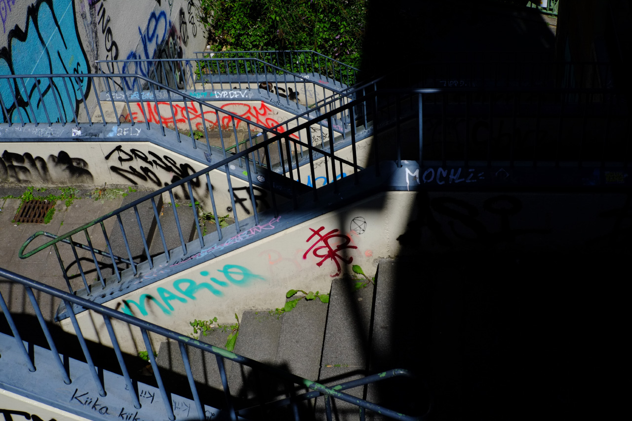 A photo of a long set of street stairs with a big dark shadow of a human to the right laying over them.