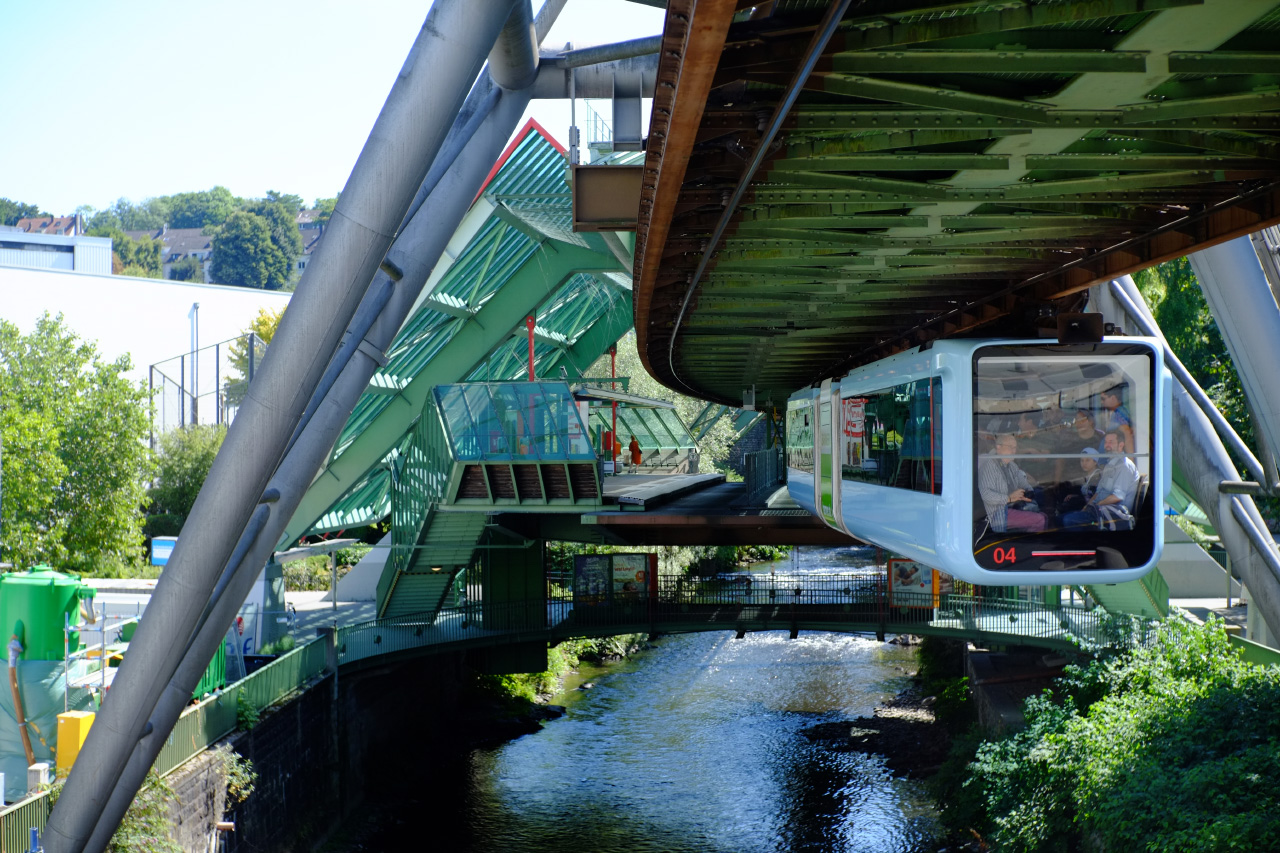 A photo of a blue suspension train car in motion above a river with people sitting inside.