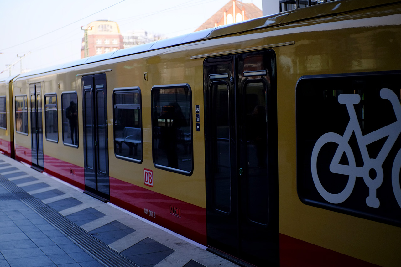 A photo of an sbahn Berlin train car: yellow with red bottom and black doors.
