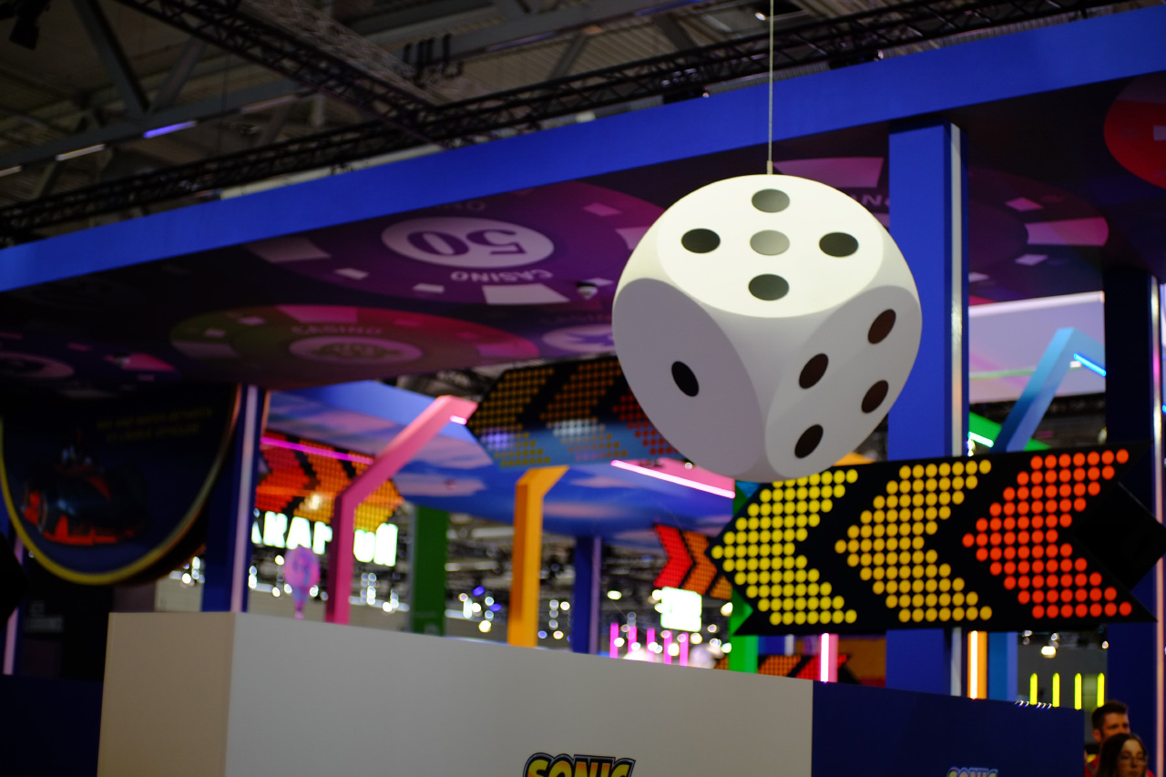 A photo of ceiling decoration of the Sonic Racing CrossWorlds booth at gamescom 2025, featuring a big white six-sided die hanging on a string, and a printed tile with big poker chips of various colours and value.