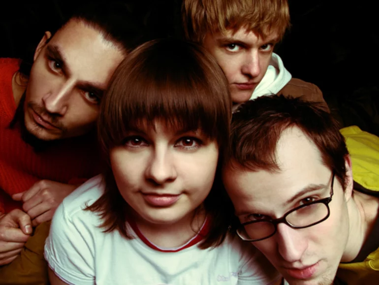 A close-up photo of four band members looking at the camera with their heads leaning on each other's heads.