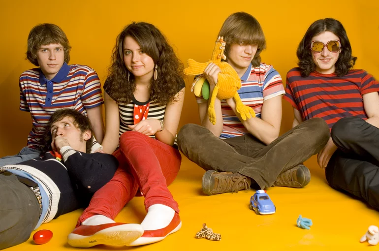 A photo of five young people on the yellow background dressed in colorful but casual attire.